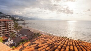 Ein Küstenhotel mit Blick auf den Strand, Reetdachgebäuden und einem Steg, der ins Meer führt.