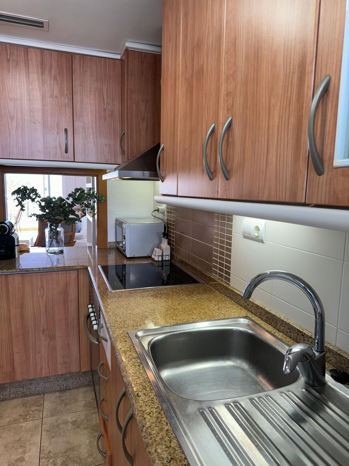 A kitchen with wooden cabinets, a stainless steel sink, granite countertops, and a toaster.