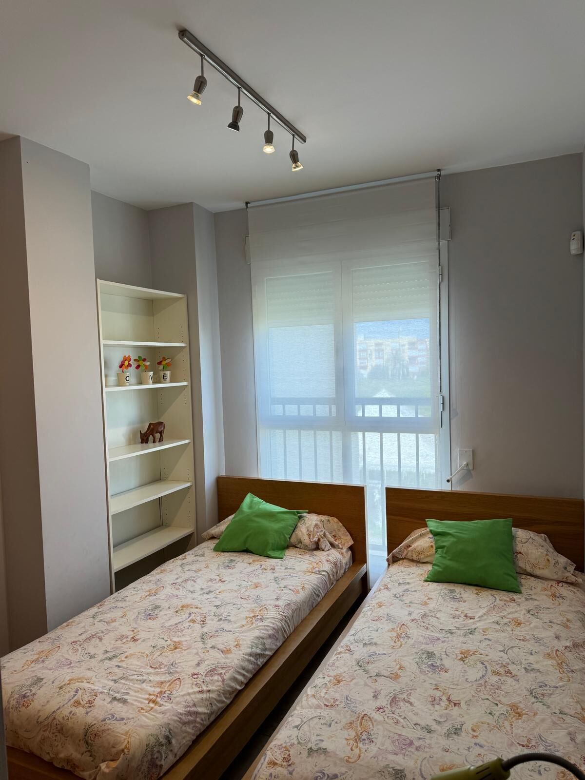 A bedroom with two single beds, a wooden headboard, a white wardrobe, and a window with blinds.