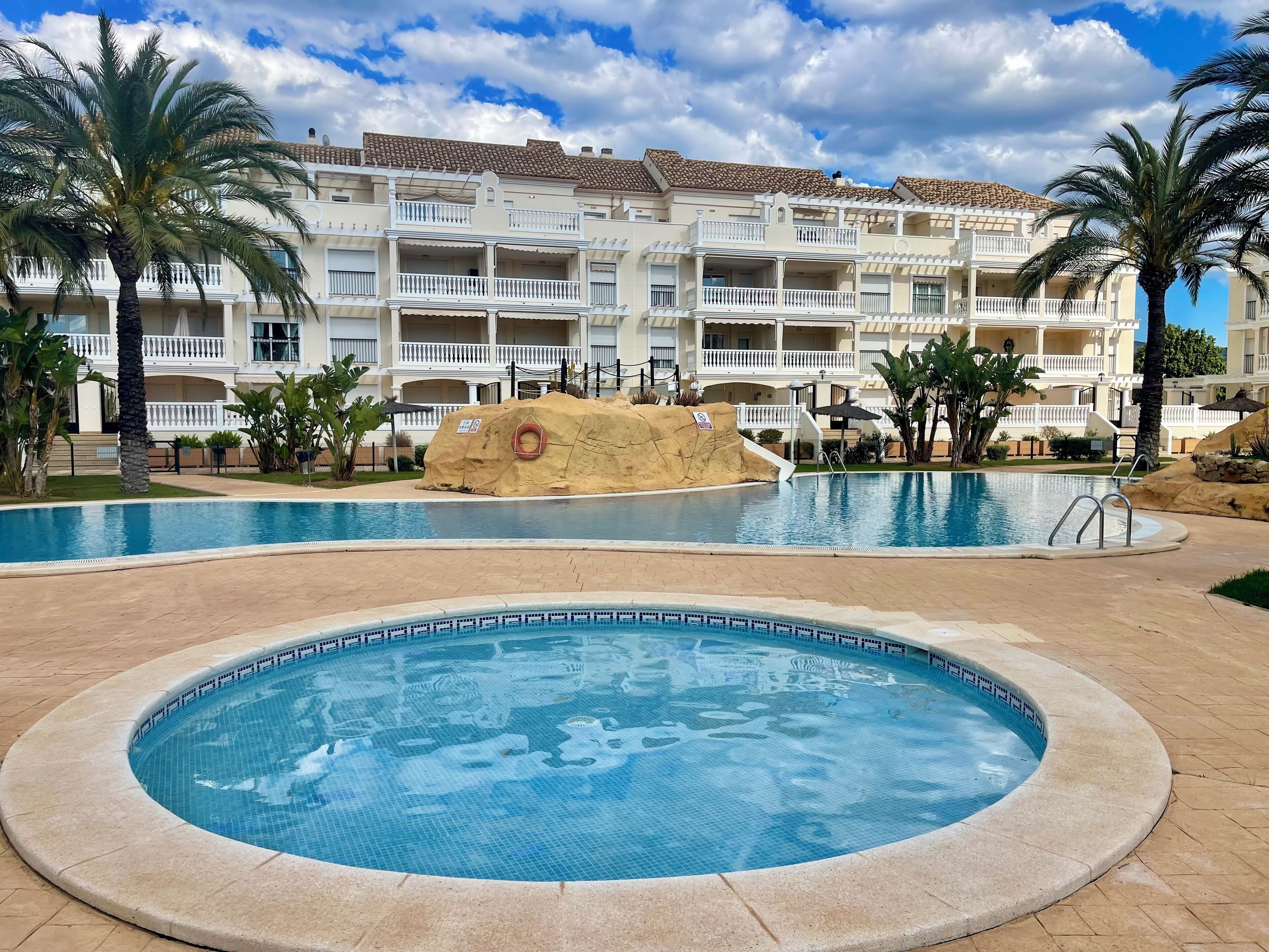 A resort with a large swimming pool, palm trees, and a building with multiple balconies.