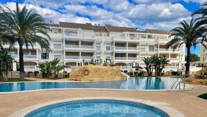 Un complexe hôtelier doté d’une grande piscine, de palmiers et d’un bâtiment agrémenté de nombreux balcons.