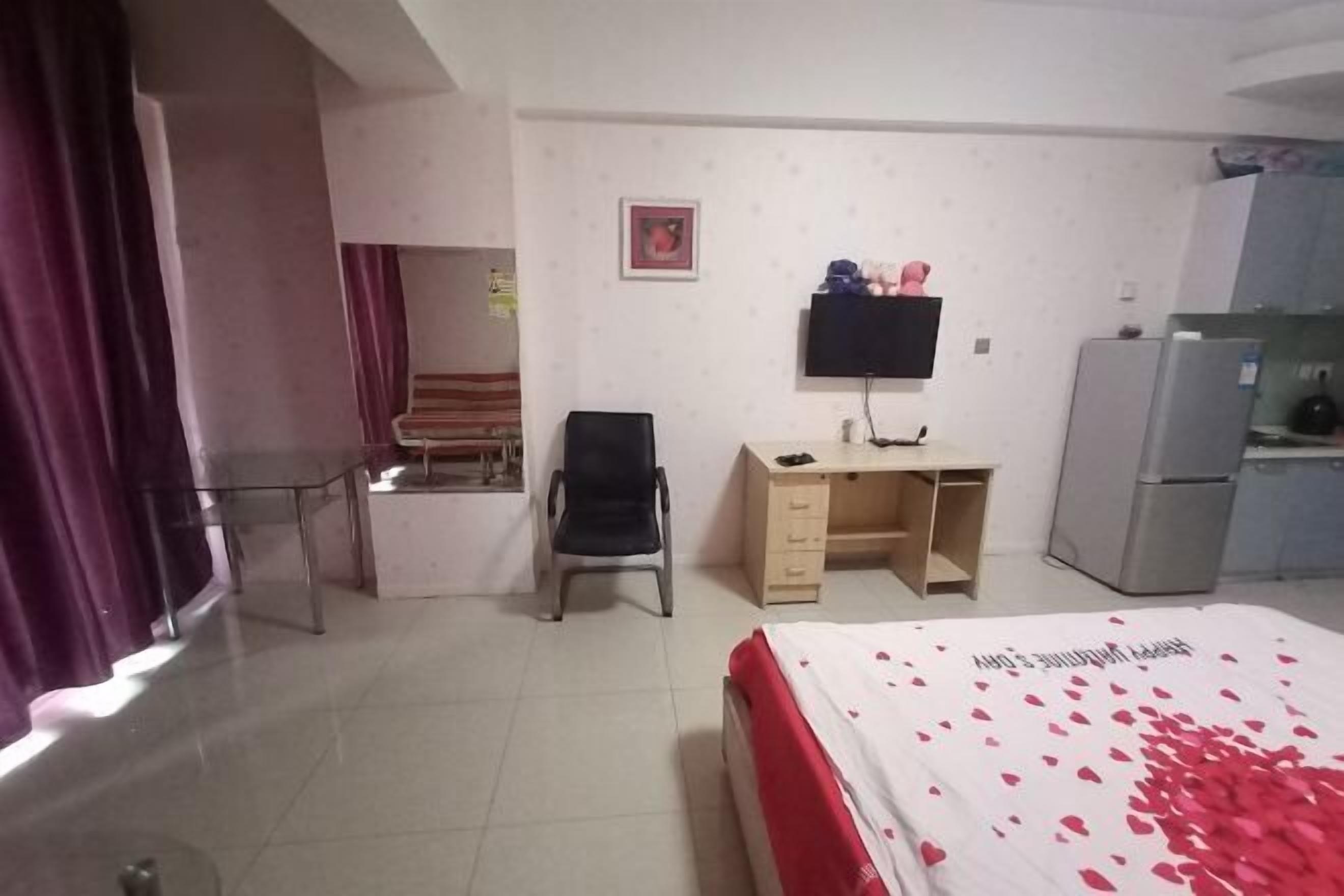 Una habitación de hotel con cama, escritorio, silla, televisor y refrigerador.