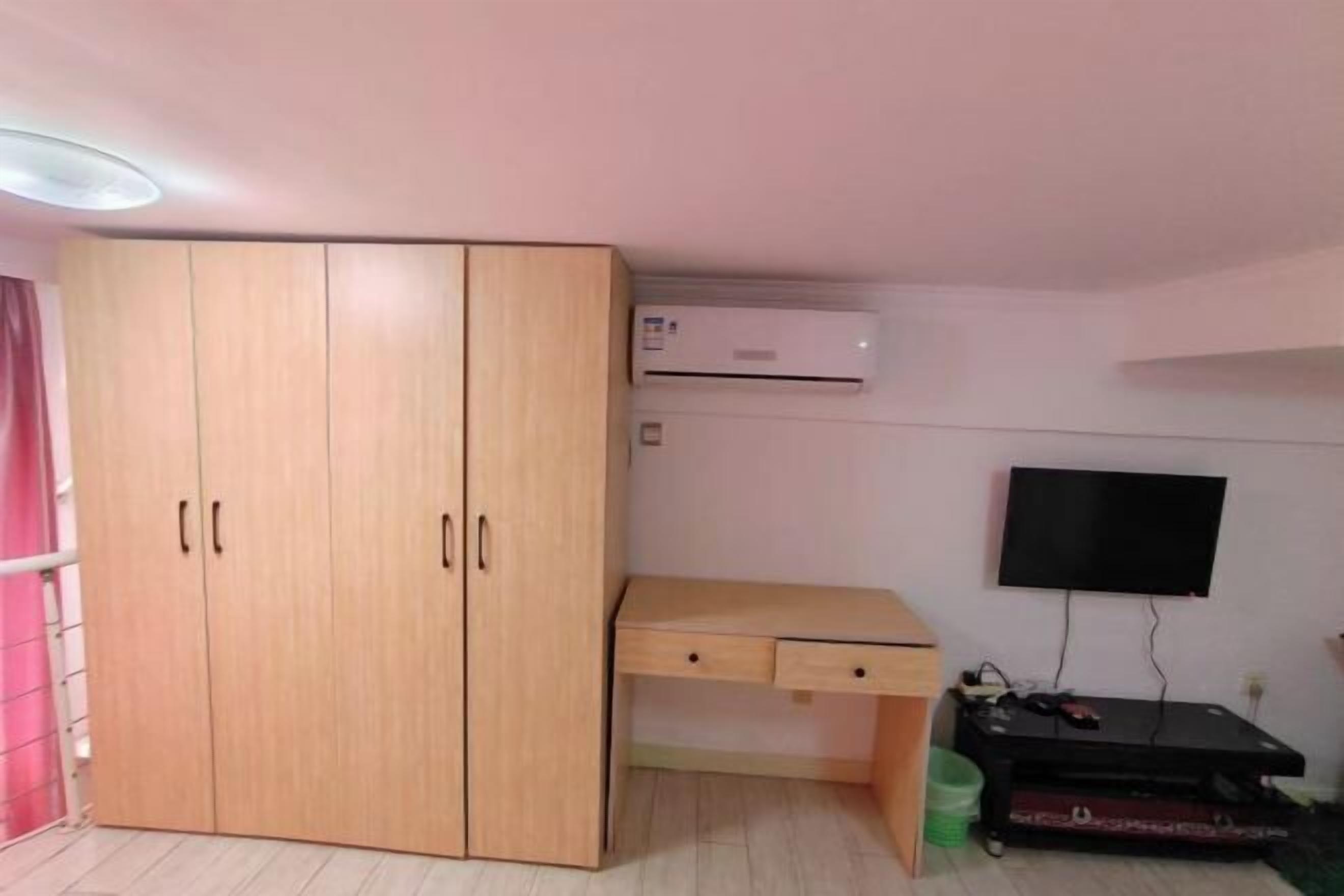 Une pièce comprenant une armoire en bois, un bureau, un téléviseur fixé au mur et un appareil de climatisation.