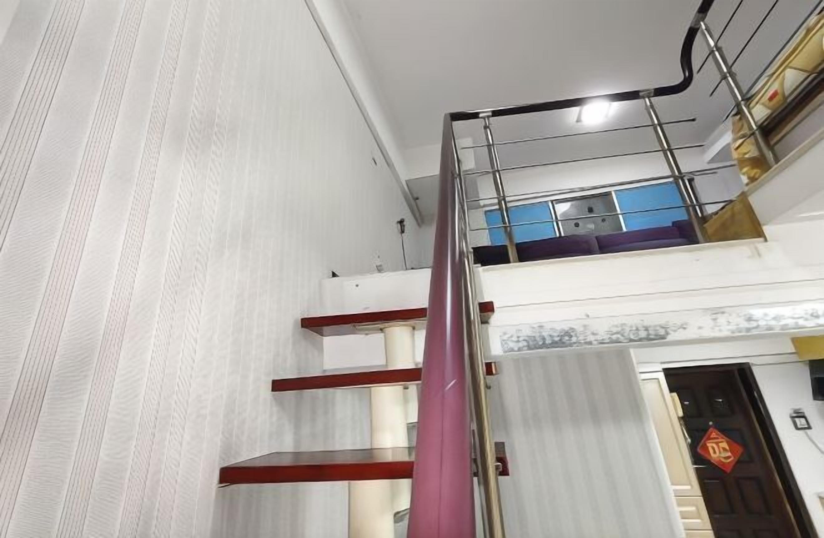 Ein mehrgeschossiges Interieur mit einer Treppe, einer Tür mit roter Dekoration und einem Fenster mit Blick auf einen blauen Himmel.