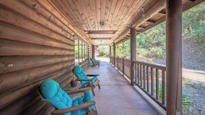 A covered porch with wooden walls and a railing, featuring several turquoise chairs and a table.