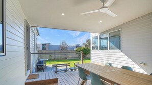 Eine überdachte Terrasse mit Tisch und Stühlen, einem Deckenventilator und Blick auf den Garten.