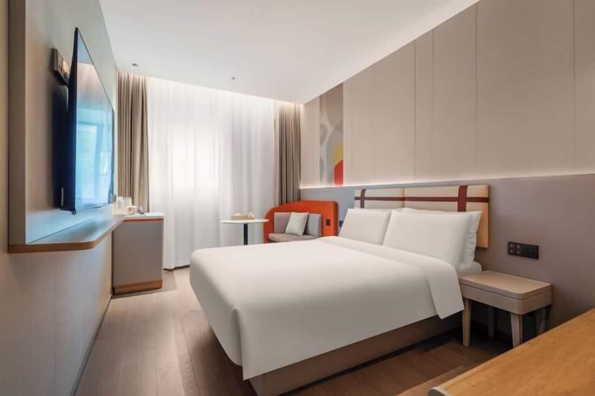 Ein Hotelzimmer mit Bett, Fernseher, Schreibtisch und Nachttisch.