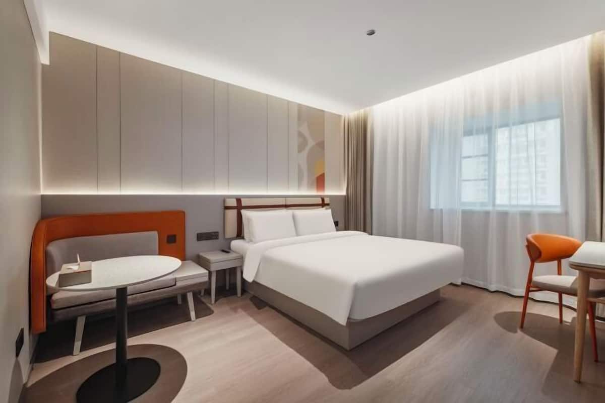 Ein modernes Hotelzimmer mit Bett, Nachttisch, Stuhl und Blick auf die Stadt durch das Fenster.