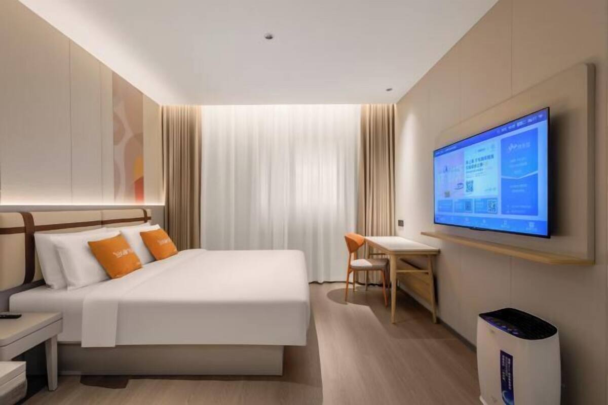 Ein Hotelzimmer mit Bett, Schreibtisch, Stuhl, Fernseher und Mülleimer.