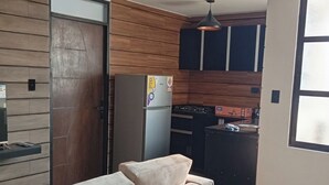 A modern kitchen with wooden paneling, a refrigerator, a stove, and a sink. There is a white sofa with cushions in the living area.