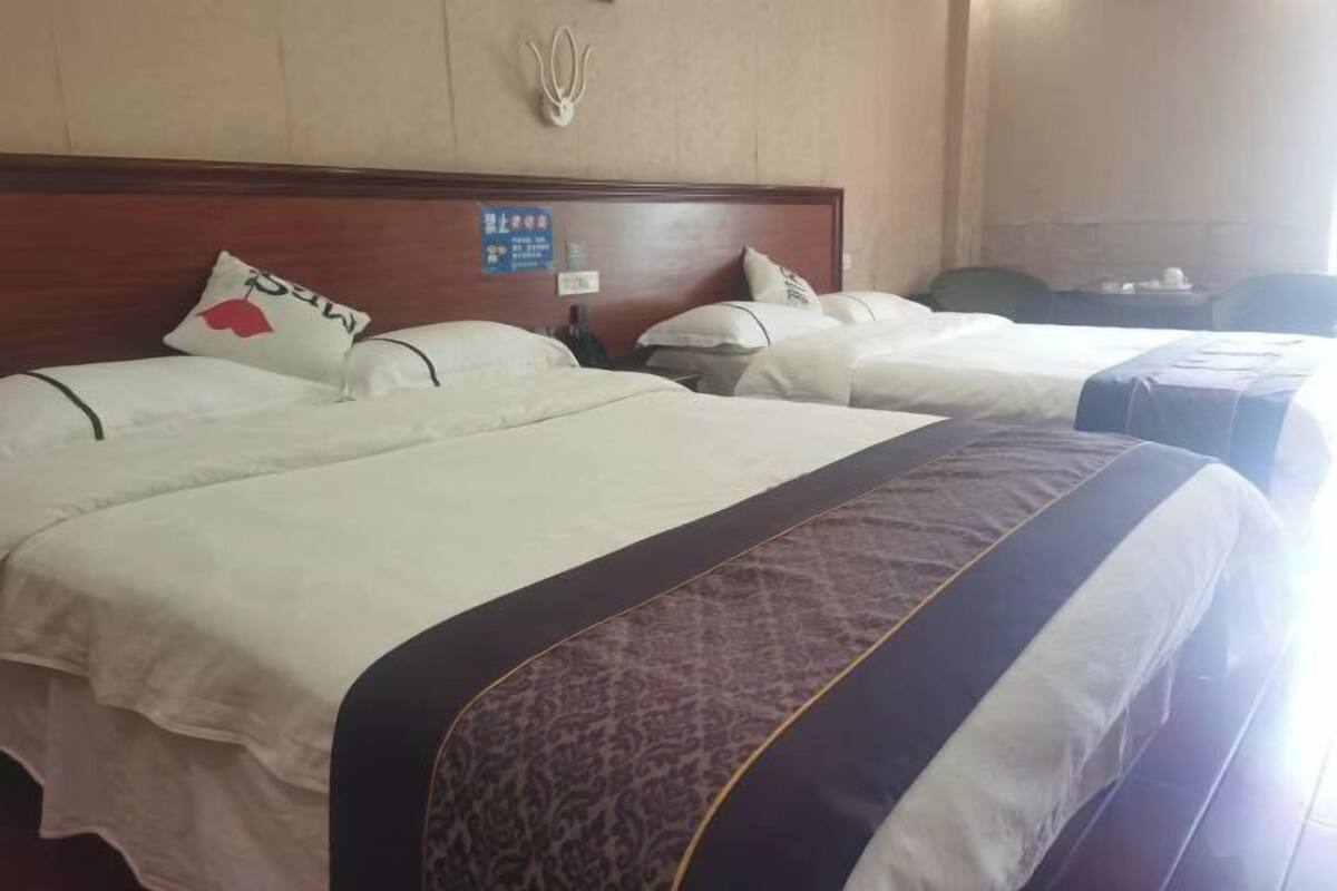 A hotel room with three beds, a wooden headboard, a wall-mounted telephone, and a sign with room information.