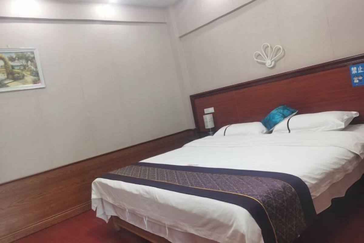 A hotel room with a bed, a nightstand, a wall-mounted light fixture, and a framed picture.