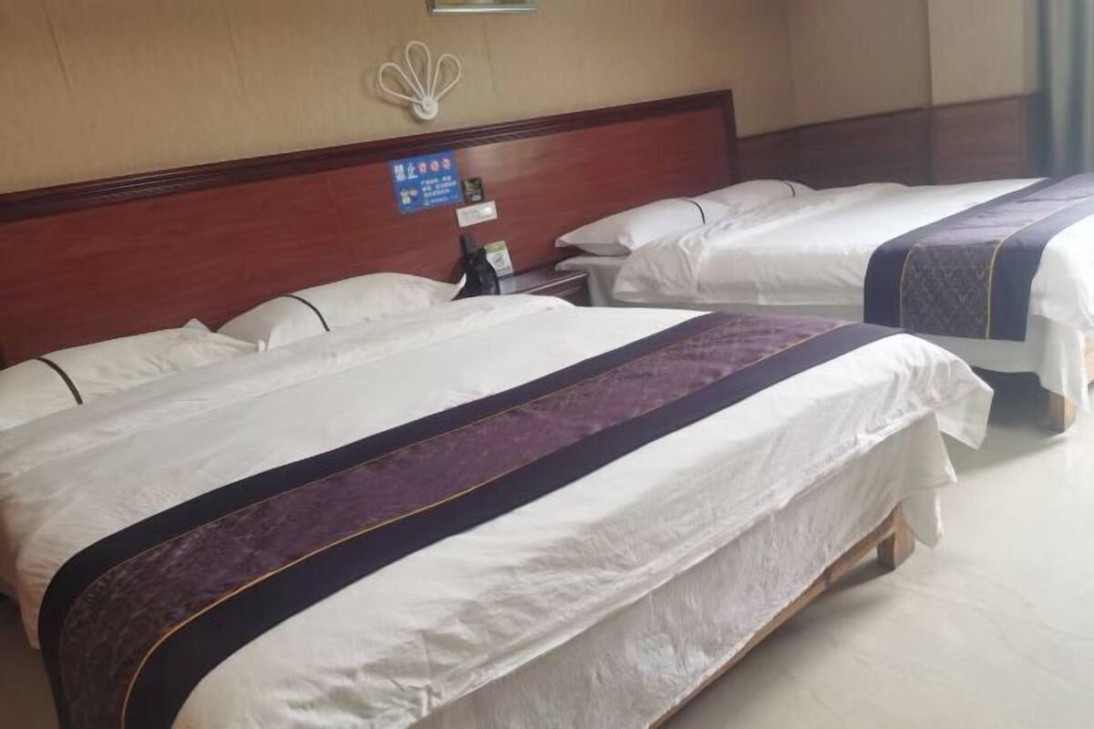 A hotel room with two beds, a wooden headboard, a nightstand, and a wall-mounted telephone.