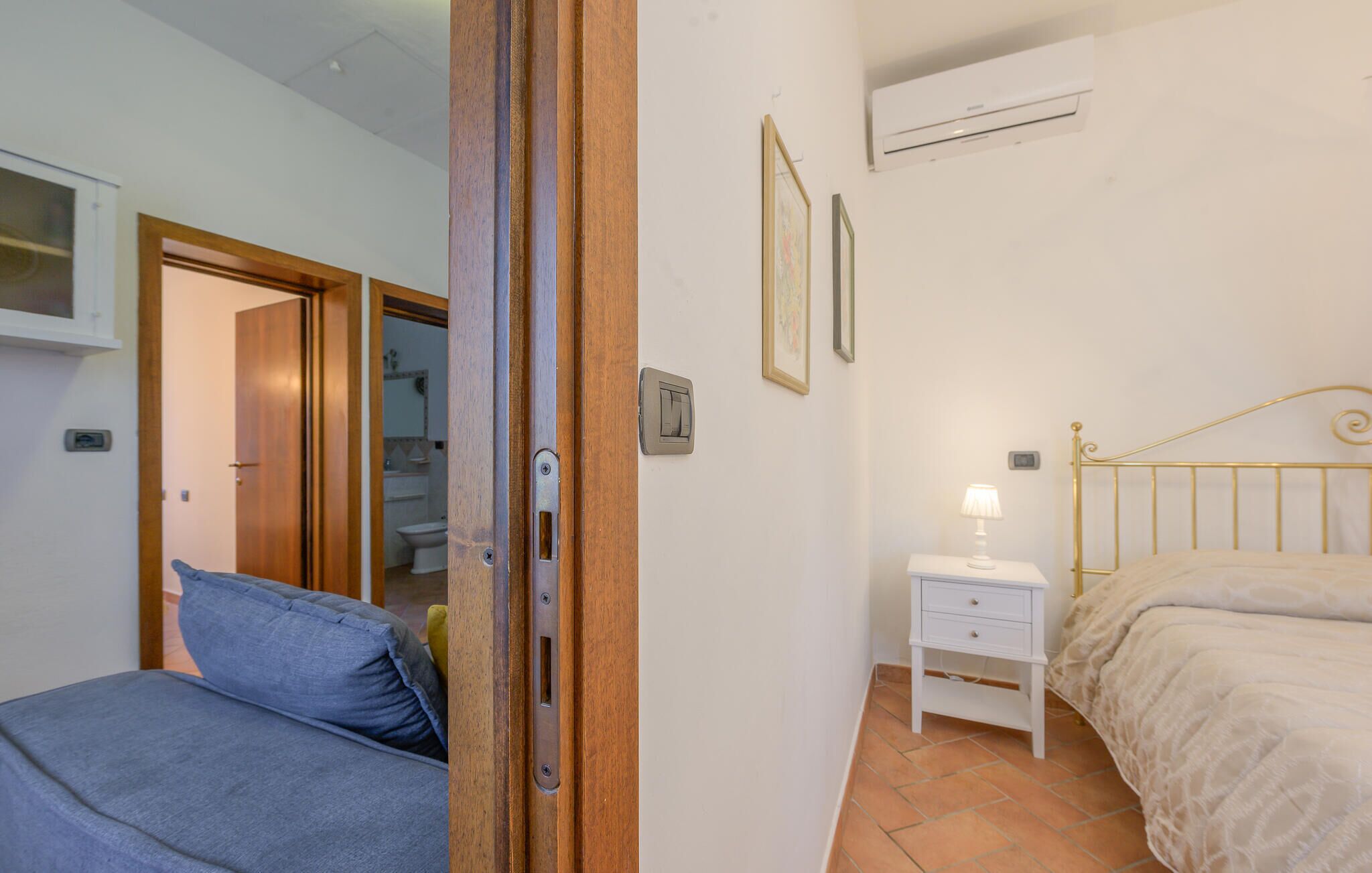 Une chambre à coucher comprenant un lit, une table de chevet, un climatiseur fixé au mur et une porte donnant sur une salle de bain.