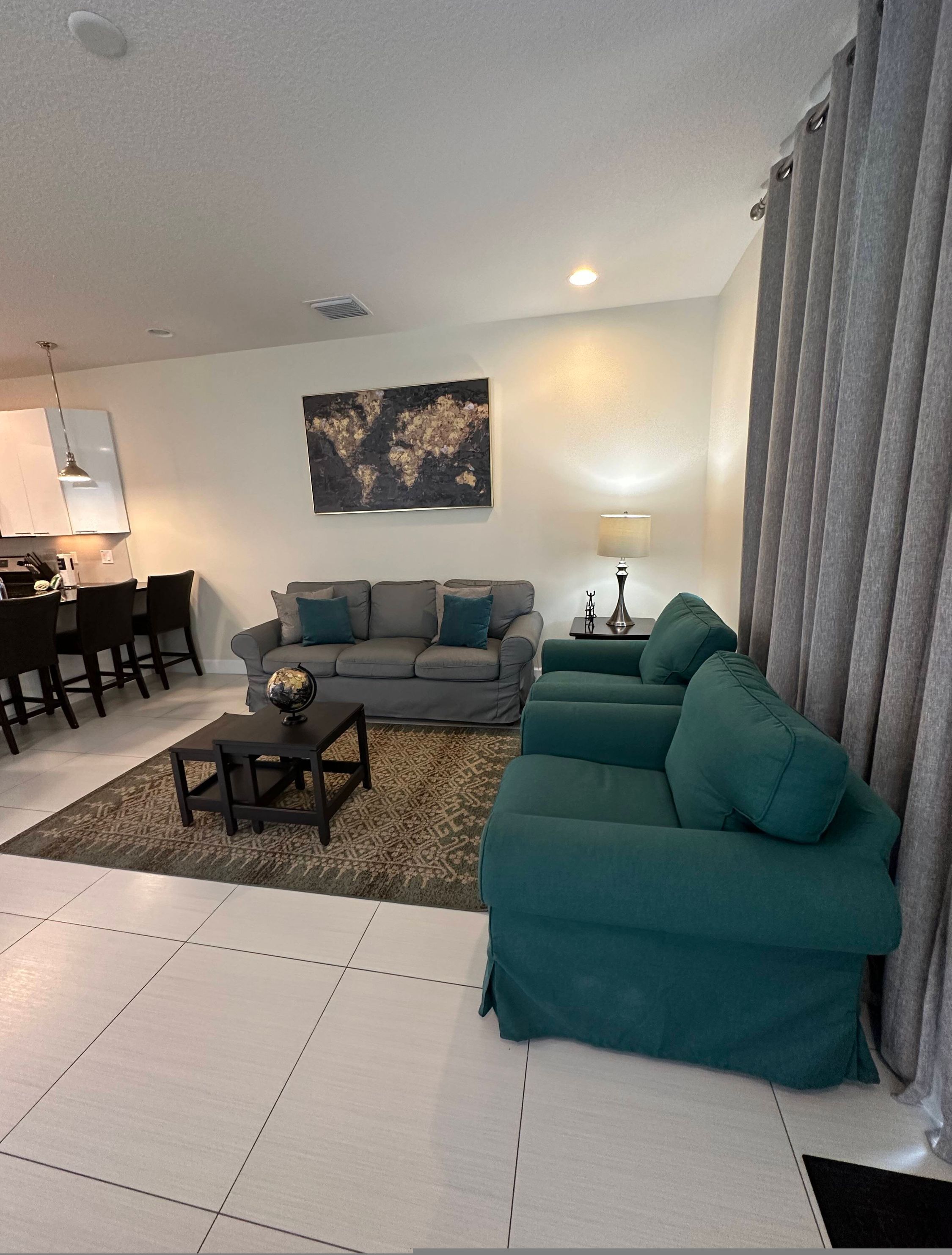Een moderne woonkamer met een grijze bank, blauwgroene fauteuils, een salontafel, en een eethoek met stoelen en een tafel.