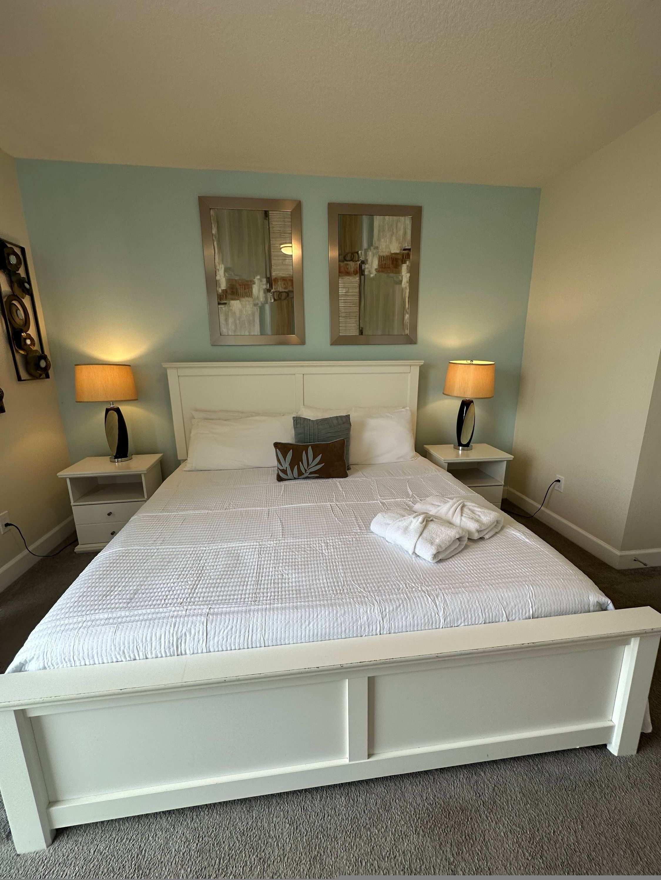 A neatly made bed with white bedding and a pillow, two bedside lamps, and a mirror on the wall.