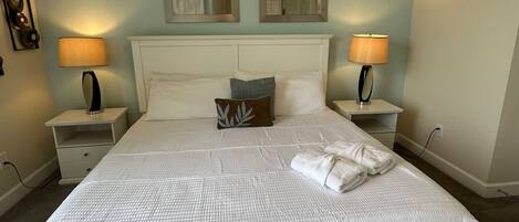 A neatly made bed with white bedding and a pillow, two bedside lamps, and a mirror on the wall.