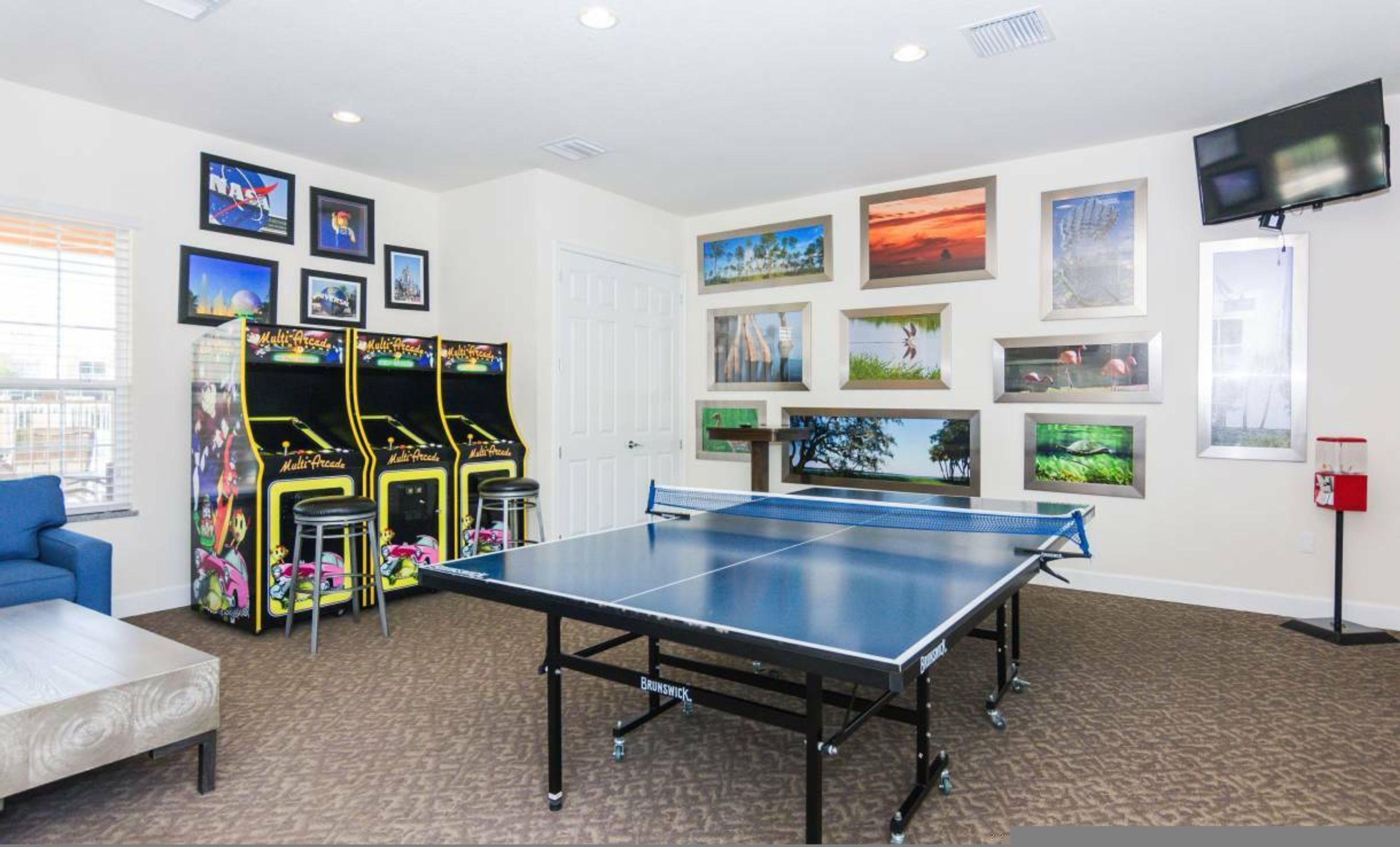 A room with a ping pong table, arcade games, and various framed pictures on the walls.