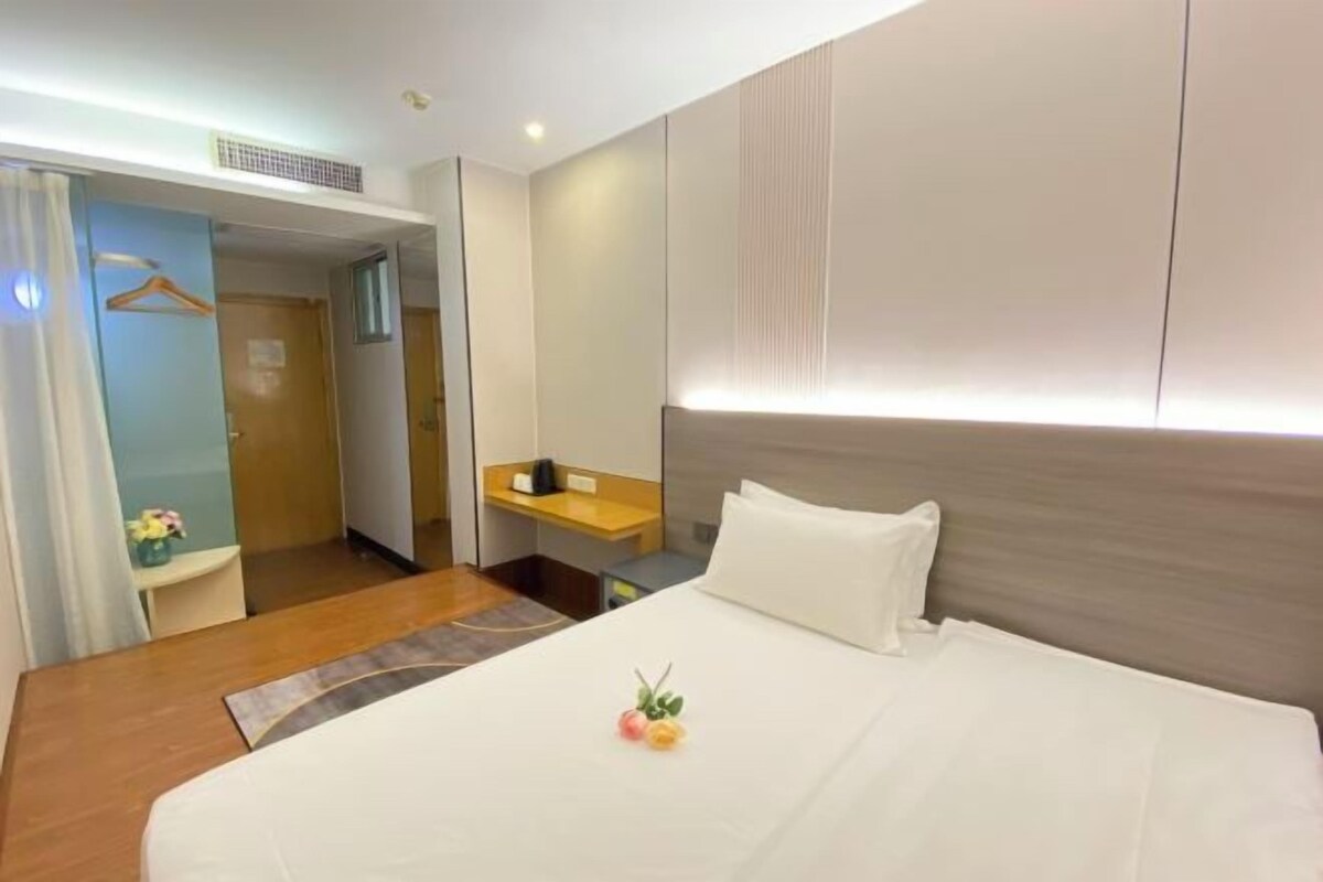 A hotel room with a bed, a bedside table, a mirror, and a door leading to another room.