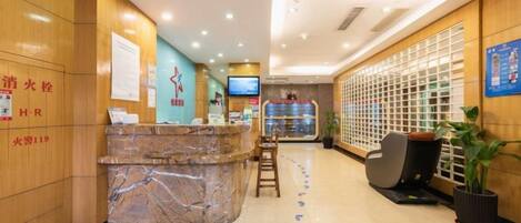 A hotel reception area with a marble counter, seating, a television, and a decorative plant.