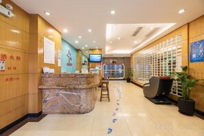 A hotel reception area with a marble counter, seating, a television, and a decorative plant. - ZhuXing Hotel (Guangzhou)