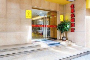 A hotel entrance with a glass door, a potted plant, and a red sign on the wall. - ZhuXing Hotel (Guangzhou)