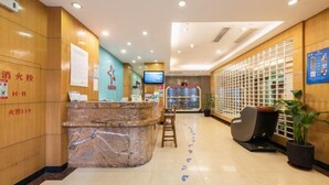 A hotel reception area with a marble counter, wooden walls, a television, and a seating area with a plant. - ZhuXing Hotel (Guangzhou)