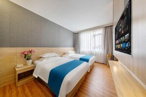 A hotel room with two beds, a small bedside table with a vase of flowers, a large flat-screen TV mounted on the wall, and a wooden bench along the window. - ZhuXing Hotel (Guangzhou)