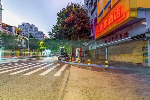 A street view with a crosswalk, a closed storefront with a red sign, and a tree in the foreground. - ZhuXing Hotel (Guangzhou)