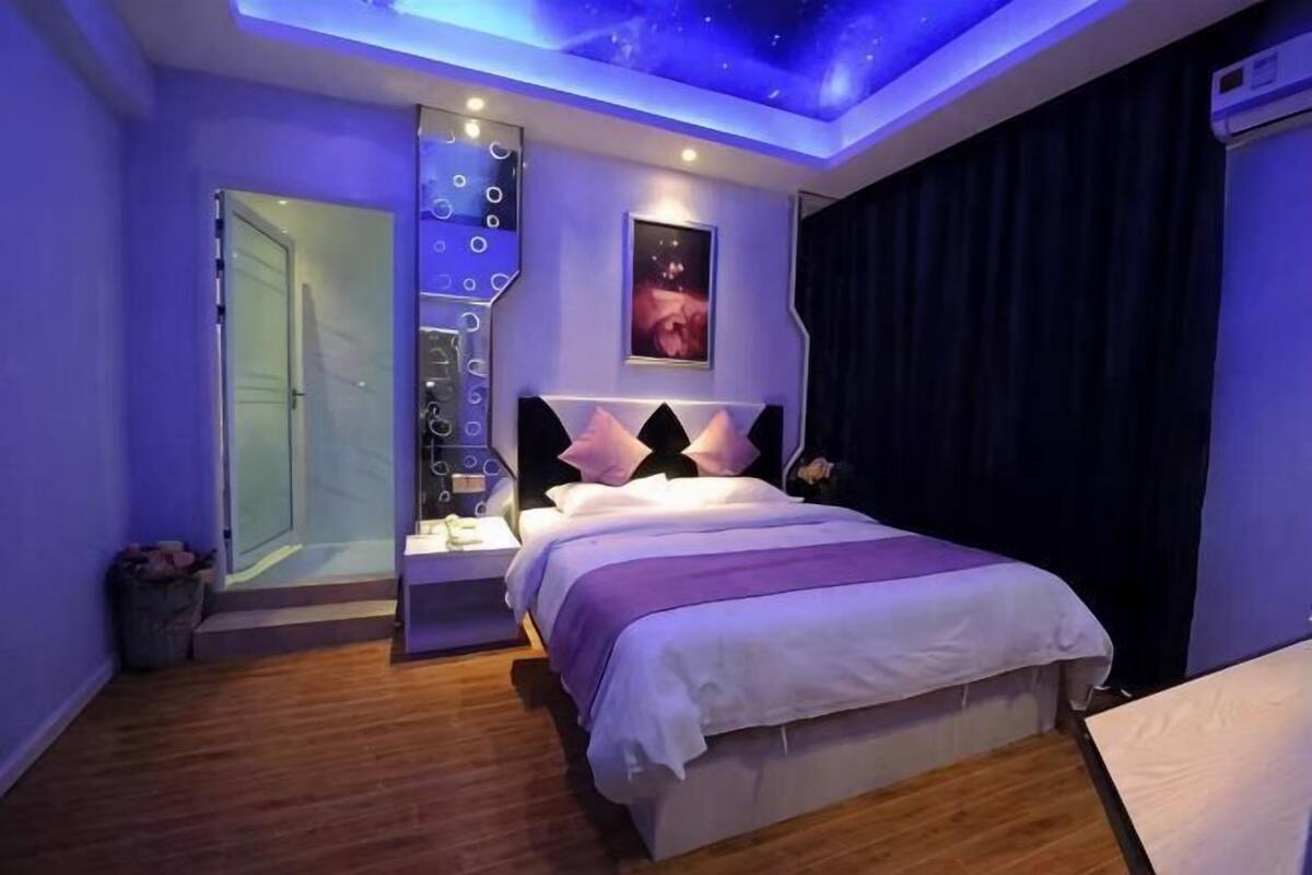Une chambre à coucher comprenant un lit, des tables de chevet, une commode, un luminaire au plafond, une fenêtre et une porte.
