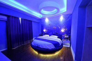 Un dormitorio moderno con cama redonda, paredes azul oscuro e iluminación ambiental.