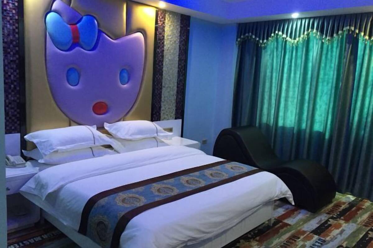 Une chambre d’hôtel avec un grand mur décoratif, un lit avec du linge de maison blanc, une chaise et un rideau.