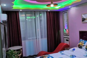 Quarto de hotel com cama, cadeira vermelha, mesinha e um vaso de planta.