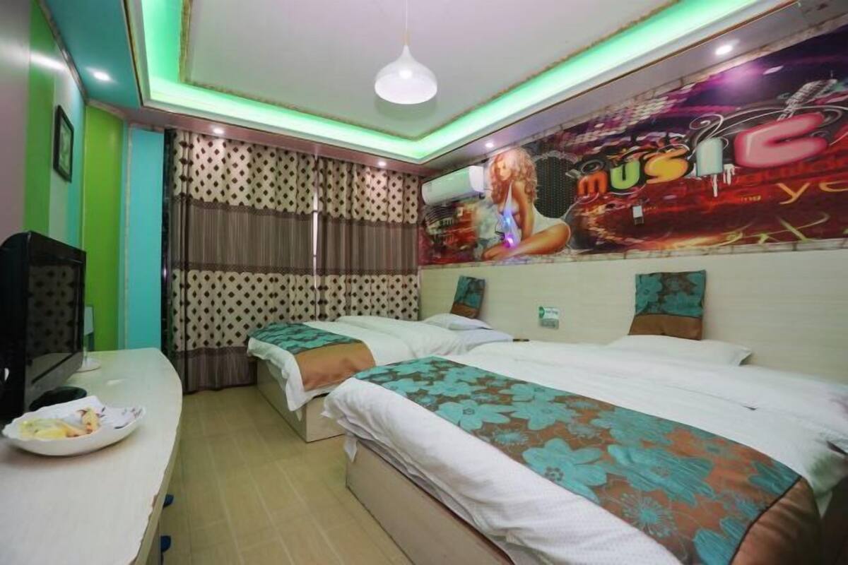 Une chambre d’hôtel avec deux lits, un bureau sur lequel se trouve une assiette de nourriture, une télévision et une fresque murale.