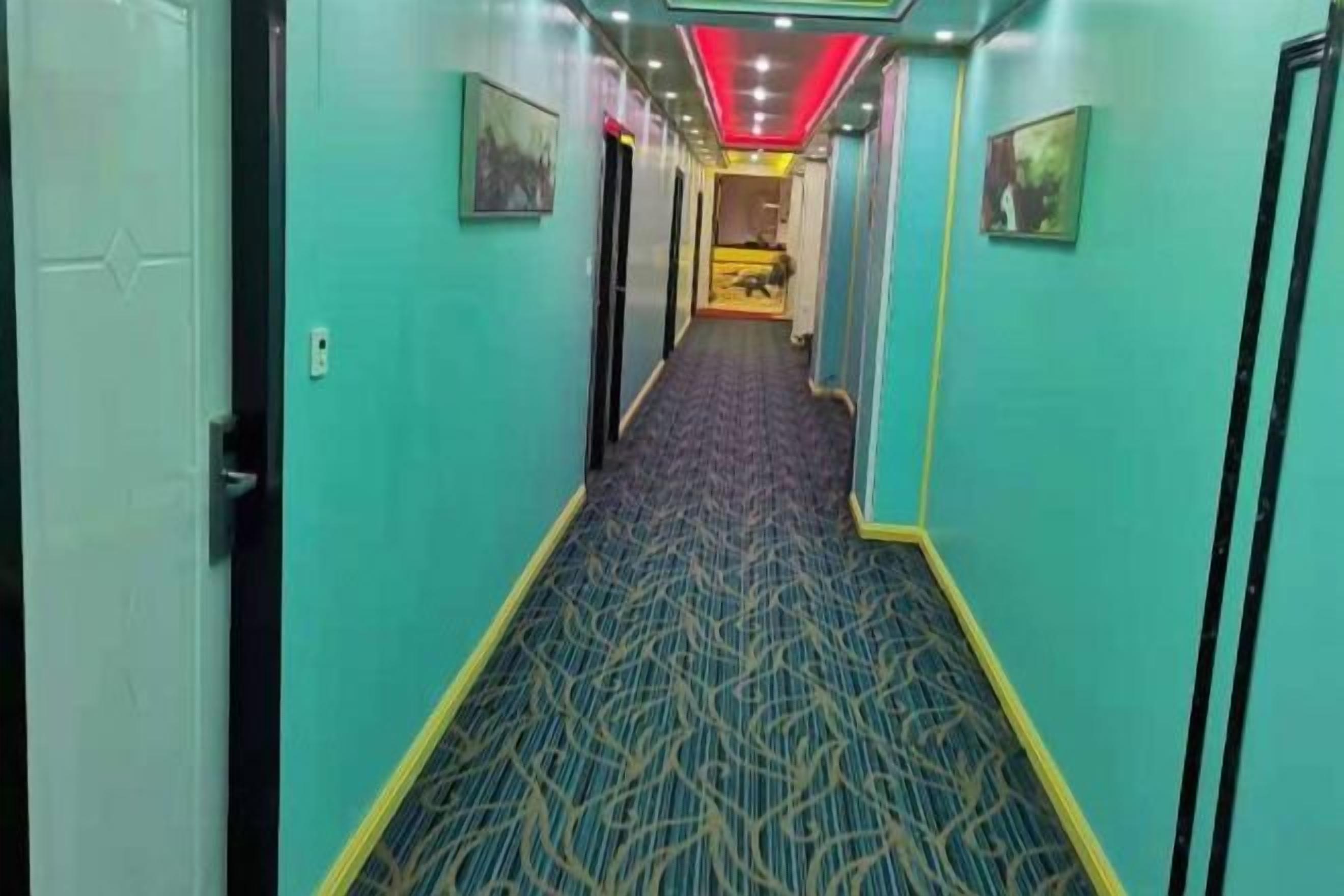 A corridor with patterned carpet, doors, and framed pictures on the walls.