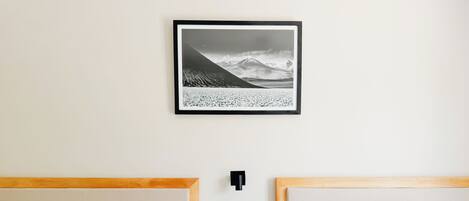 Habitación de hotel con dos camas, cada una con ropa de cama y almohadas blancas, cabecero de madera y una fotografía en blanco y negro de un paisaje montañoso en la pared.