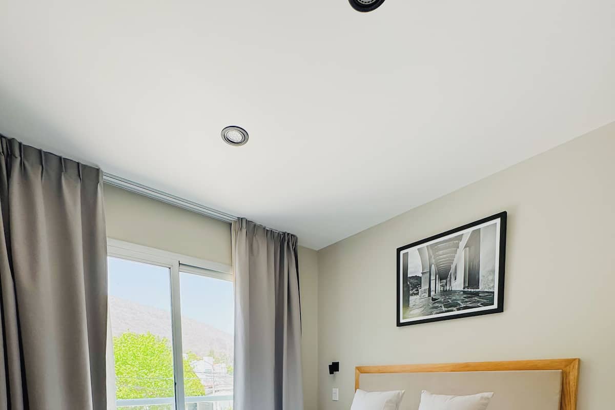 A bedroom with a large bed, a wooden headboard, a nightstand, and a window with curtains.
