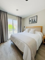 Un dormitorio con una cama grande, cabecera de madera, mesita de noche y una ventana con cortinas.