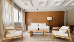 A modern living room with a white sofa, two wooden chairs, a wooden coffee table, and a floor lamp. - Casa Foresta (Salta)