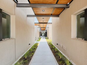 A modern corridor with a concrete pathway flanked by grass and plants, leading to a building entrance. - Casa Foresta (Salta)