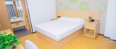 A hotel room with a bed, bedside table, and a small desk with a chair.