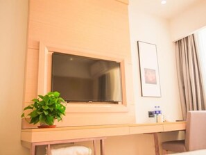 A hotel room with a flat-screen TV mounted on the wall, a potted plant on a side table, a framed picture on the wall, and a window with curtains. - Greentree Inn Yangzhou Jiangdu Xiaoji Town South Zhongxing Road Express Hotel (Yangzhou)