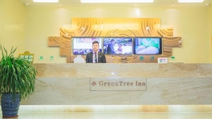 A reception desk at GreenTree Inn with a marble counter, two monitors displaying images, and a potted plant to the left.