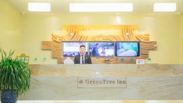A reception desk at GreenTree Inn with a marble counter, two monitors displaying images, and a potted plant to the left.