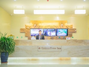 A reception desk at GreenTree Inn with a marble counter, two monitors displaying images, and a potted plant to the left. - Greentree Inn Yangzhou Jiangdu Xiaoji Town South Zhongxing Road Express Hotel (Yangzhou)
