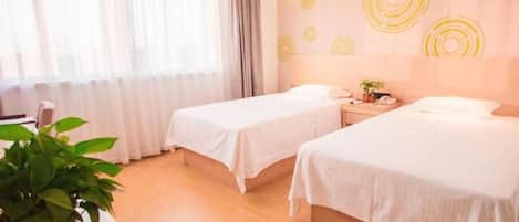 Habitación de hotel con dos camas, una mesita de noche, una planta y una ventana con cortinas.