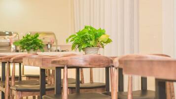 A row of wooden chairs with cushioned seats and backs, arranged in a dining area with a potted plant on a table.