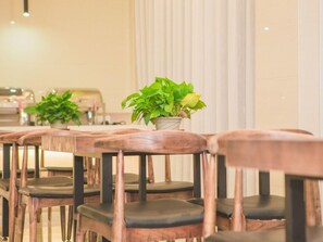 A row of wooden chairs with cushioned seats and backs, arranged in a dining area with a potted plant on a table.