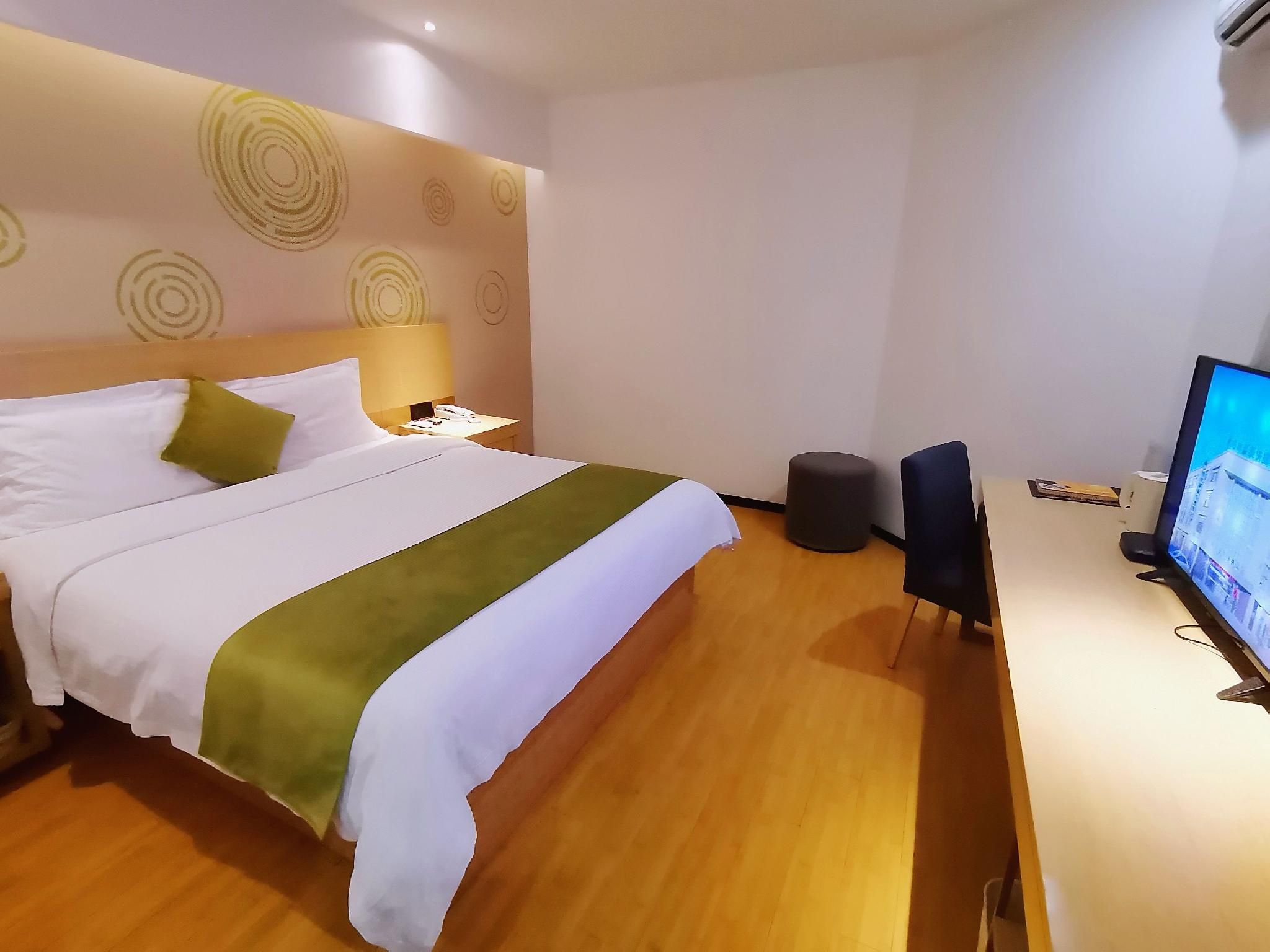 A hotel room with a bed, bedside table, lamp, and a desk with a computer monitor.