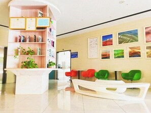 A reception area with a white reception desk, colorful chairs, a bookshelf with various items, and framed pictures on the wall.